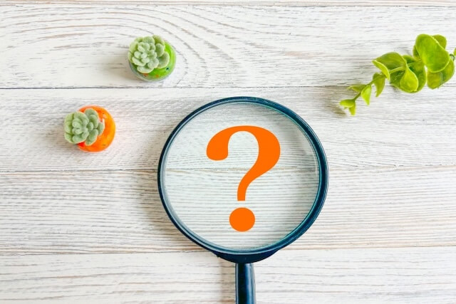 白い木目に置かれた虫眼鏡とクエスチョンマーク