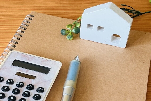 ノートに置かれた電卓と家型ブロック