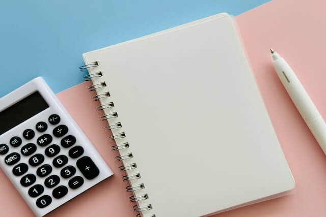 ピンクと水色の背景に置かれたノートと電卓