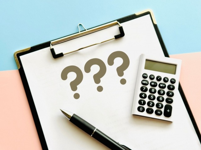 クエスチョンマークが書かれた書類と電卓
