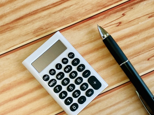 木目テーブルに置かれた電卓とボールペン