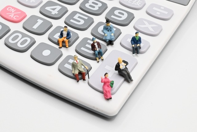 電卓のボタンに座る小さなフィギュアたち