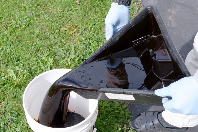 廃油をバケツに移す作業員の男性