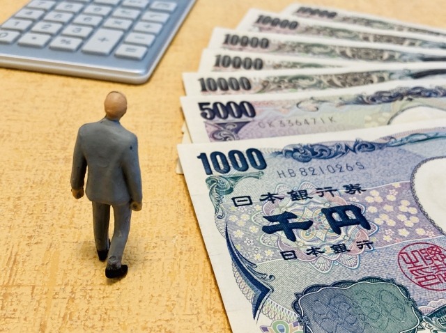 お金と電卓を眺める男性の人形