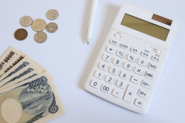 白い机に置かれた電卓とお金