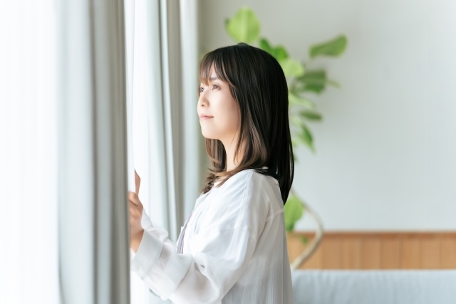 白いカーテンを開ける女性