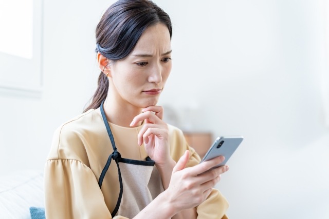 スマホを見て悩むエプロン姿の女性