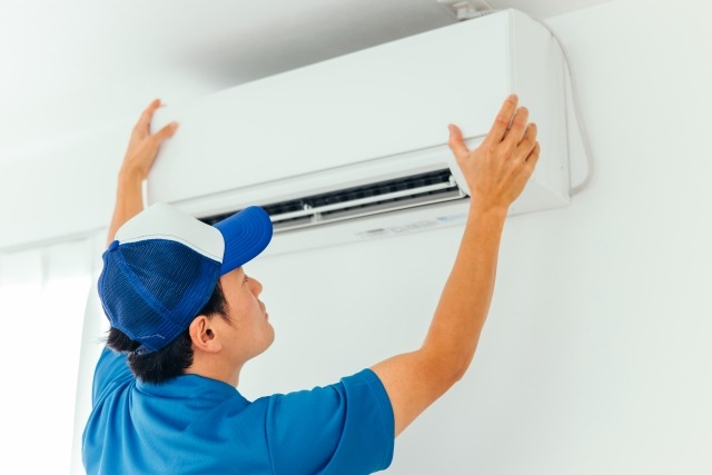 エアコンに触れる青い作業着を着た男性