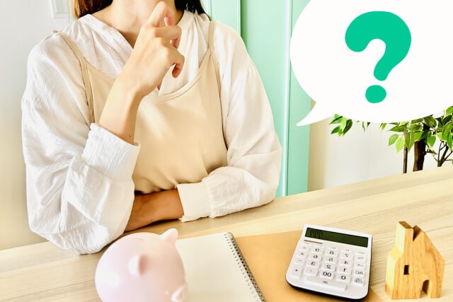 電卓や貯金箱の前で考える女性