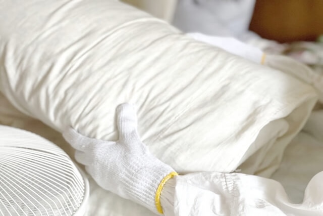 丸めた布団を抱える軍手の作業員