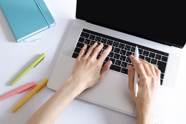 手帳を横に置いてパソコンで作業する手元の画像