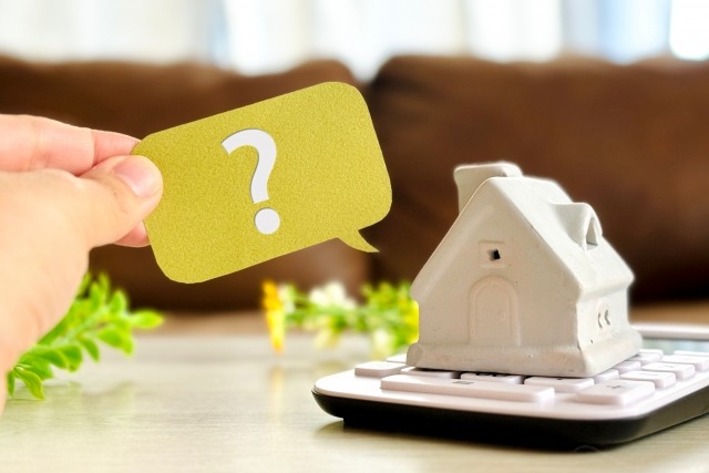 電卓に乗せたミニチュアの家とクエスチョンマーク