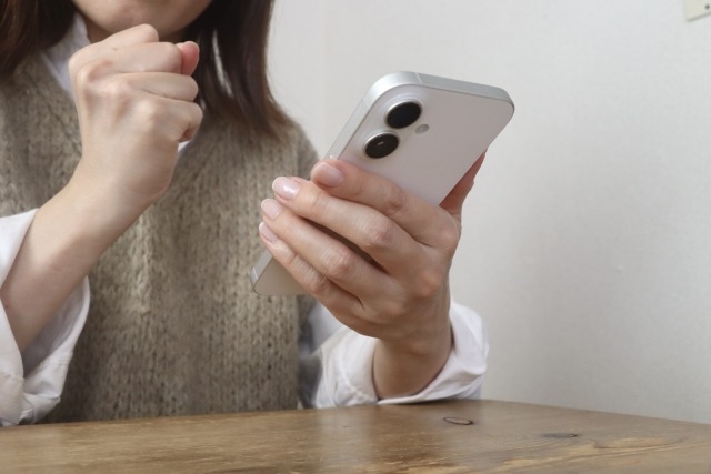 スマホを見て拳を握りしめる女性