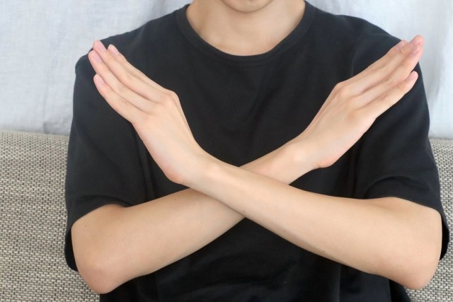 腕でバツを作る黒いTシャツの男性