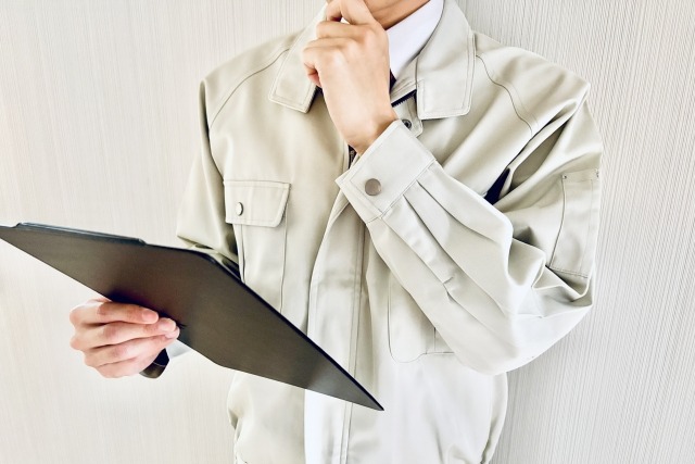 バインダーを見て悩む作業服の男性