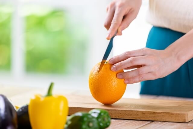木製まな板の上で包丁でオレンジを切る様子