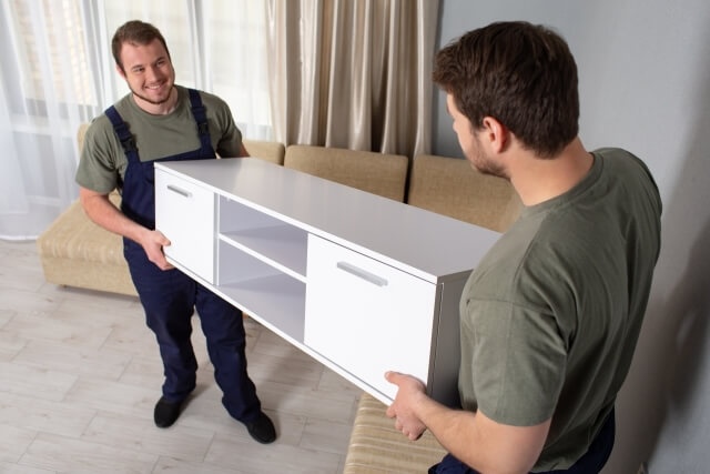 白いテレビ台を運ぶ男性2人の画像