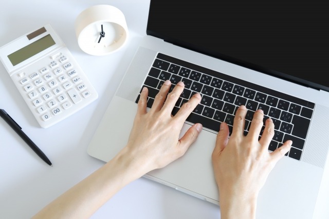 デスクでパソコンと電卓を広げる様子