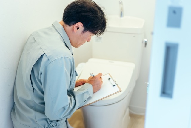 作業服の男性がトイレの前で点検する様子
