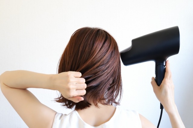黒いドライヤーで髪を乾かす女性