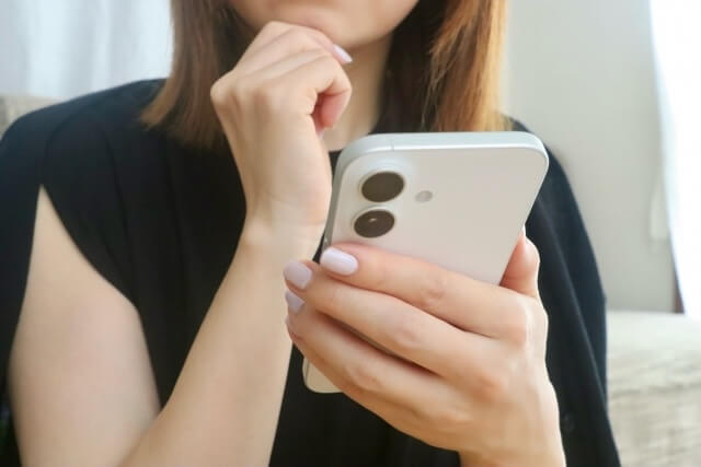 スマホ画面を見て悩む女性